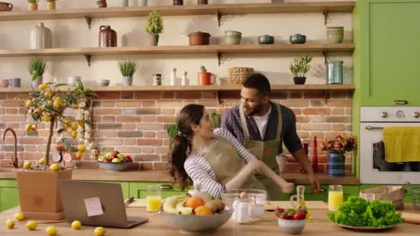 In a large modern kitchen happy with a large smile multiracial couple enjoy the time while cooking the dinner they dancing and playing together — ストック動画