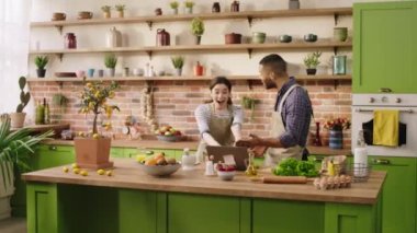 Good looking woman getting excited while she looking over the laptop in the kitchen together with her boyfriend she start to jump and hugging her partner Afro American man