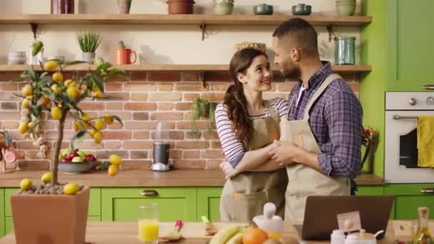 Modern kitchen island multiracial couple very handsome looking dancing while preparing the breakfast together then woman looking something on the laptop and getting very excited start to clapping — Stockvideo