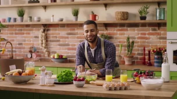 Улыбаясь большой молодой привлекательный афро-американец на своем острове на кухне позирует перед камерой и смотрит прямо улыбается широко — стоковое видео