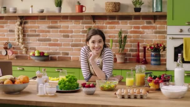 Fröhliche charismatische Frau am Morgen auf der Kücheninsel, die vor der Kamera breit lächelt und sich beim Zubereiten des Essens aufgeregt fühlt — Stockvideo
