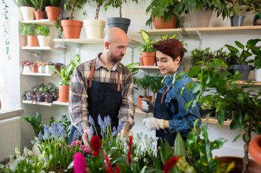 Çiçekçide not defteri olan meslektaşının yanında önlüklü bir çiçekçi dizüstü bilgisayar tutuyor.