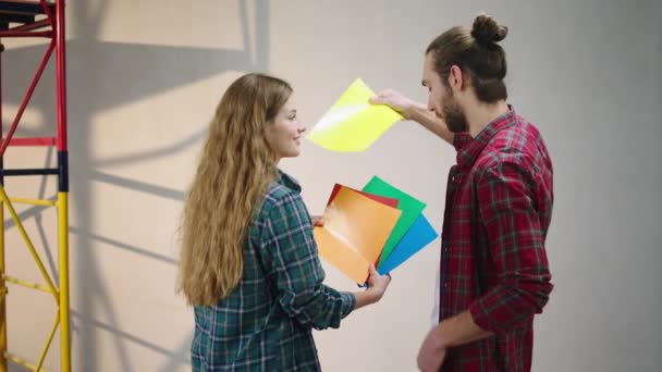 Karismatisk och snygg par hemma tillsammans analysera färgpaletten för att välja den bästa att måla väggen i sitt vardagsrum — Stockvideo