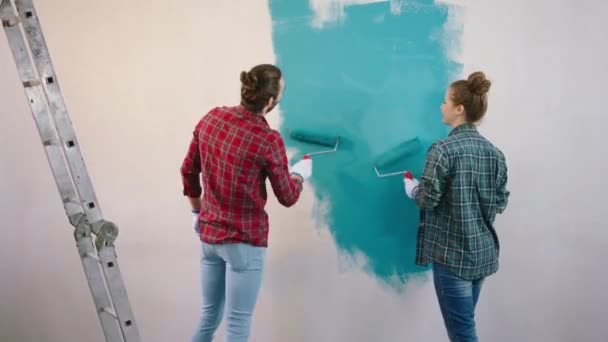 Bem parecido jovem casal em casa pintura em azul a sala de estar eles sorrindo grande e usando o rolo escova de parede para o trabalho — Vídeo de Stock