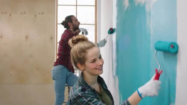 Em casa mulher carismática e seu marido caucasiano olhando paredes de pintura em uma cor azul sorrindo grande e se sentindo feliz trabalhando juntos — Vídeo de Stock