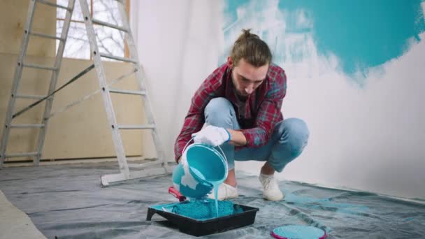 Bell'uomo che usa un po 'di colore per mettere in un contenitore speciale per dipingere le pareti in un colore blu a casa che lavora concentrato — Video Stock