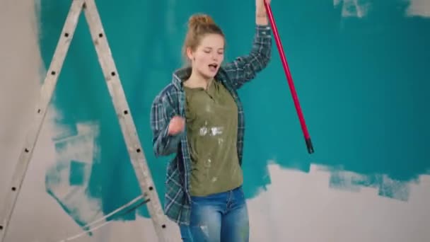 Belle femme chantant en dansant avec un rouleau à brosse murale à la maison elle se sent heureuse après avoir fini de peindre les murs — Video