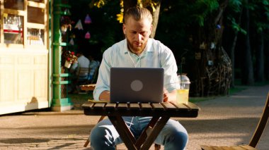 Sakallı ve arkaya kıvırcık saçlı yakışıklı bir adam parkta bir masada oturmuş kulaklıklarıyla müzik dinlerken ciddi işler yapıyor. PORTRAİT