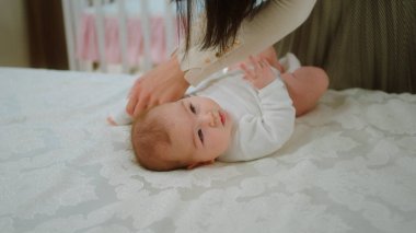 Yatak odasında, küçük tatlı bir kız bebek. Genç annesiyle hız yapıyor. Bebeğe sıkıca sarılıyor ve birlikte oynuyor..