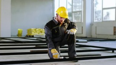 Özel üniforma ve güvenlik kaskıyla inşaat alanında dans eden bir inşaat işçisi inşaat malzemeleri boyuyor ve aynı zamanda kablosuz kulaklıklardan müzik dinliyor ve dans ediyor.