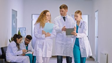 Başhekim yetişkin adam ve meslektaşı genç iki kadın doktor hastane koridorunda yürüyorlar ve tabletten hastalarının test sonuçlarını analiz ediyorlar.