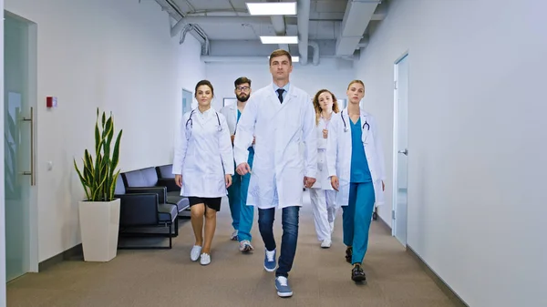 Big team of doctors and nurses multiethnic in the hospital corridor walking in front of the camera straight. Portrait