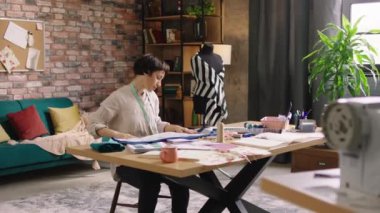 Küçük işletme atölyesi moda tasarımcısı güzel ve çok karizmatik moda tasarımcısı kadın terzi atölyesinde mutlu çalışıyor. Ölçüm yapmak için birkaç kumaş alıyor.