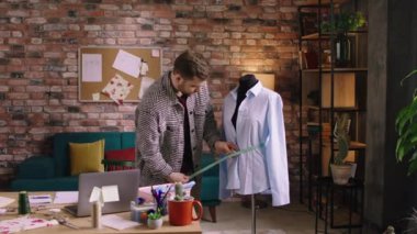 Kareli ceket giyen bir adam bir mankenin belini ölçüyor ve ev ofisindeki ölçümleri not alıyor. ARRI Alexa Mini 'de çekilen