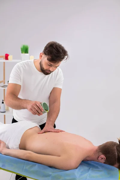 At spa salon the professional masseur man add some oil massage on back of his client and massage slowly the muscles while the client are laying down on the massage table. Detail