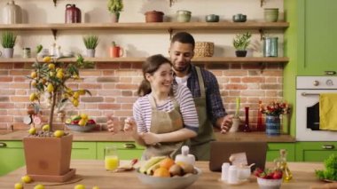 Birlikte yemek hazırlarken mutlu ve heyecanlı bir çift mutfak adasında dans ediyor ve büyük bir gülümsemeyle anın tadını çıkarıyor. 4k