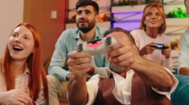 Bir grup iş arkadaşı mavi fasülye koltuklarında rahatça oturuyor ve birbirlerine vurmaya çalışırken konsolda dinleniyorlar. 4k