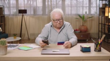 Okul kamerasının önünde iyi görünümlü, konsantre bir ihtiyar akıllı telefondan online bir şeyler sipariş ediyor evde internet üzerinden ödeme yapmak için kredi kartını kullanıyor. 4k