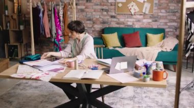 İş yerindeki kıyafet tasarımcısı kadın renk paletini ve kumaşlarını analiz ederek yeni kıyafetler yaratıyor. Bazı yeni modeller çizmeye hazırlanıyor. Atış açık.