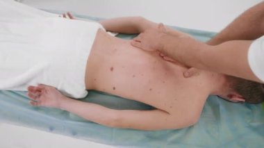 Klinikte rahatlama ve sağlıklı vücut kavramı. Terapist, sırt masajı yapan bir adama masaj yapıyor. Vücuda yoğun masaj yapıyor. ARRI Alexa Mini 'de çekilen