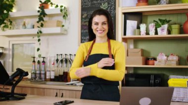 Kameranın önünde baristaya poz veren kocaman bir gülümseme ve modern bir kahve dükkanında el ele tutuşan bir kadın. ARRI Alexa Mini 'de çekilen.