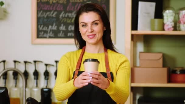 在现代咖啡店里 一位漂亮的女人拿着一杯生态咖啡 当着她的面对着摄像机 — 图库视频影像