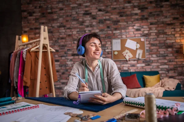 . Modern tailoring atelier woman fashion designer very charismatic working and listening music from headphones at her workplace she make some sketch on her new collection