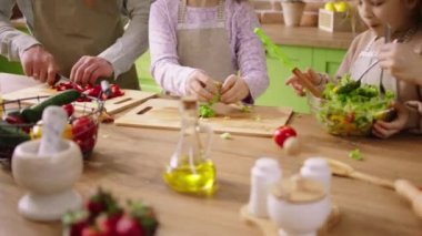 Heyecanlı aile üyeleri birlikte sağlıklı bir kahvaltı hazırlıyorlar salata için taze sebzeleri kesiyorlar ve birlikte vakit geçiriyorlar..