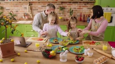 Evde, mutfakta, mutlu aile fertleri ve iki güzel küçük kız dans ederken ve birlikte kahvaltı hazırlarken heyecanlanırken yemek için tabağa biraz salata ekliyorlar. 4k