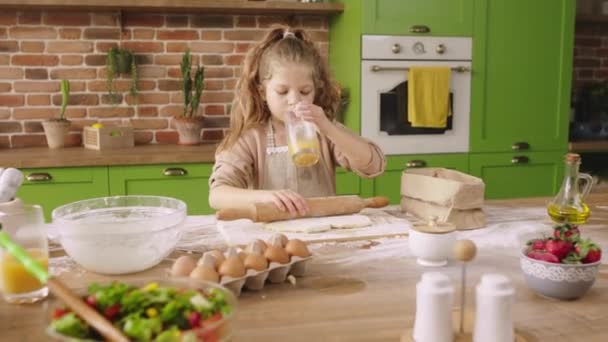 在现代化的乡村厨房岛上 一个漂亮的长发姑娘一个人在鼓吹美味的甜点 她端着她的杯子喝着新鲜的橙汁 — 图库视频影像