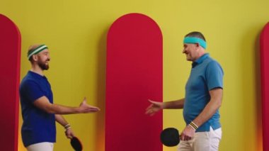 İyi görünümlü iki masa tenisi oyuncusu pinpon oynamaya başlamadan önce el sıkışıyor sonra da kameranın önünde büyük bir gülümsemeyle ve el ele tutuşarak poz veriyor. 4k