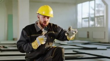 Şantiyedeki karizmatik inşaat işçisi kablosuz kulaklıklardan müzik dinlerken şarkı söylemek ve dans etmek için boya fırçası kullanıyor. 4k