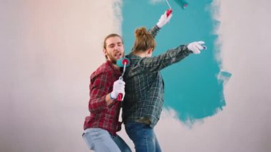 At home funny crazy couple very charismatic while painting walls make a break and start dancing and singing with the wall brushes.