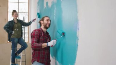 Geniş, geniş bir oturma odası. Birlikte mutlu çalışan beyaz bir çift. Duvarları mavi renge boyuyorlar. 4k