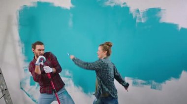 Dans eden heyecanlı beyaz çift duvarları boyarken eve bakıyor fırça rulosuyla dans ediyorlar ve tuhaf hareket ediyorlar. 4k