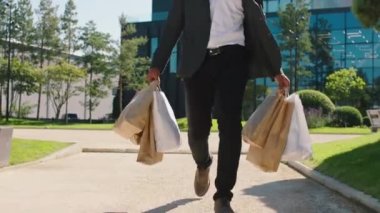 Alışveriş merkezinden siyah bir adam sokakta yürürken video görüntüsü alıyor. Elinde bazı ekolojik alışveriş torbaları var..