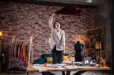 Küçük işletme atölyesi moda tasarımı. Güzel kadın moda tasarımcısı. Ofisinde dans ediyor, kanepeye zıplıyor ve iş yerinde eğleniyor. Portre