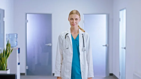 Happy young woman family doctor looking straight to the camera and have a good mood in the hospital corridor.