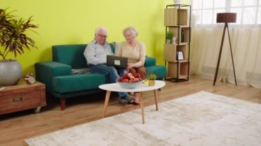 Evde kanepede yan yana otururken internetten alışveriş yapmak için yaşlı sevgilisiyle birlikte dizüstü bilgisayar kullanıyor. 4k