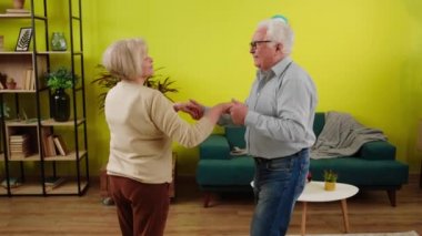 Handsome old man and his wife very beautiful woman dancing together in the living room at home they enjoy the time together.