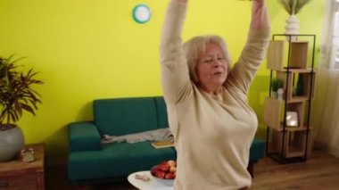 Excited and charismatic old woman in living room happy dancing and jumping while she is alone at home she have a healthy lifestyle. Shot on ARRI Alexa Mini