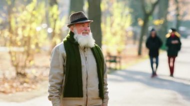 Büyük bir parkta, kocaman gülüşü olan yakışıklı yaşlı bir adam, bir sonbahar günü yürür ve eski moda bir şapka giyer. ARRI Alexa Mini 'de çekilen.