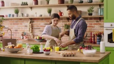 Gülümseyen karizmatik kadın ve partneri birlikte yemek hazırlıyorlar. Mutfak adasında taze ve sağlıklı bir salata yapıyorlar. 4k