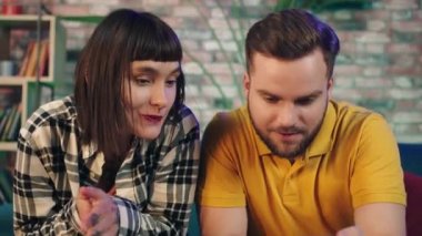 In front of the camera charismatic couple very excited watching a sport match on the smartphone concentrated they spending time together at home on the sofa. Shot on ARRI Alexa Mini
