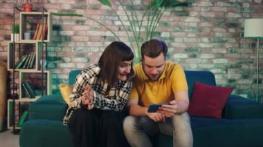 Oturma odasında heyecanlı bir çift akıllı telefondan maç izliyor. Takımları kazandığında ve zafer kazandıklarında mutlu oluyorlar.