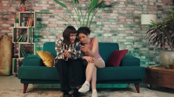 Two Charismatic Ladies Home Sofa Watching Something Smartphone Together Spending — Wideo stockowe