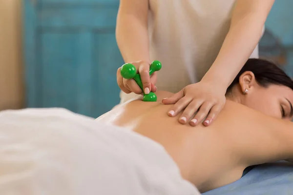 Professional massage room the therapist woman using special massage accessories for a revitalising back massage happy client laying down on the massage table.