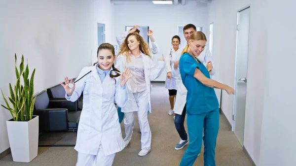 Hospital stuff group of doctors and nurses in front of the camera dancing excited and looking straight to the camera they have large smile.