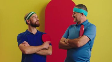 Charismatic and good looking two men old and young posing in front of the camera with a large smile crossing hands they are table tennis players before game posing to the camera. 4k