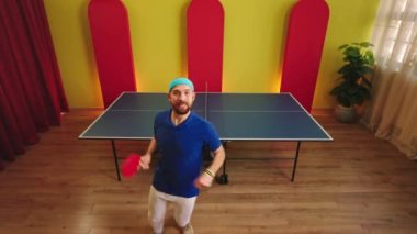 Kameranın önünde dans eden yakışıklı adam elinde raketiyle masa tenisi oynamaya hazırlanıyor..